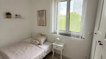 Helles Kinderzimmer mit Einzelbett, Laminatboden und Fenster mit Blick ins Grüne.