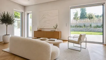 Helles Wohnzimmer mit großen Fenstern, modernem Sofa und Blick in den Garten.