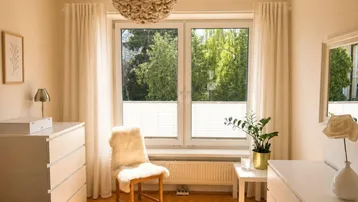Helles Schlafzimmer mit Holzboden, großem Fenster und Blick ins Grüne, ausgestattet mit modernen Möbeln.