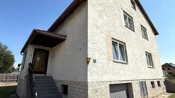 Vorderansicht eines Einfamilienhauses mit Außentreppe und Garagenzufahrt unter blauem Himmel.