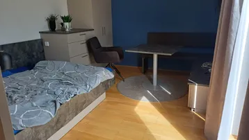 Helles Schlafzimmer mit Holzboden, blauer Akzentwand und kleinem Essbereich.