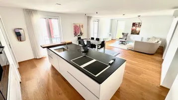 Moderne offene Wohnküche mit Kücheninsel, Essbereich und hellem Wohnzimmer mit Holzboden.