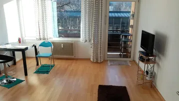 Helles Wohnzimmer mit Laminatboden, großen Fenstern und Zugang zum Balkon.