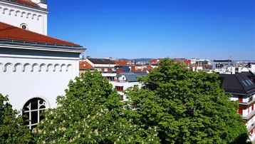 Panoramablick über die Stadt mit grünen Bäumen und einem historischen Gebäude unter blauem Himmel.