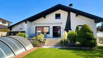 Rückseite des Hauses mit gepflegtem Garten, Rasenfläche und überdachtem Poolbereich unter blauem Himmel.