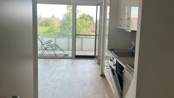 Offener Wohnbereich mit integrierter Küche, Parkettboden und Zugang zu einem sonnigen Balkon.
