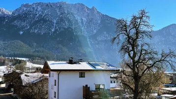 Weißes Wohnhaus mit schneebedecktem Dach und Balkon vor beeindruckender Bergkulisse.