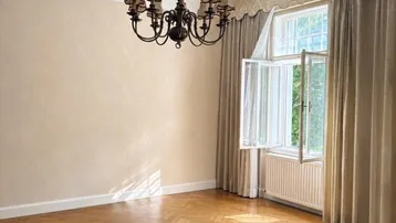 Helles Zimmer mit Fischgrätparkett, Stuckdecke und klassischem Kronleuchter, bereit zur individuellen Gestaltung.