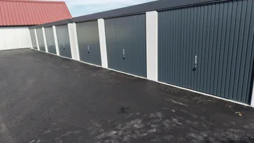 Moderne Garagenreihe mit dunklen Toren und heller Fassade, umgeben von einer neuen asphaltierten Zufahrt.