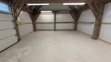 Geräumige Garage mit Holzbalkenkonstruktion, Betonboden und großem Sektionaltor.