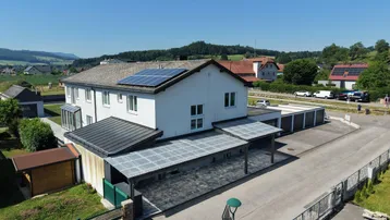 Luftaufnahme eines Hauses mit Photovoltaikanlage, Carports und ländlicher Umgebung.