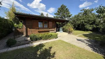 Gemütliches Holzhaus mit gepflegtem Garten und sonniger Terrasse unter blauem Himmel.