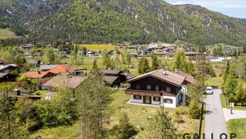 Luftaufnahme eines Hauses im alpinen Stil mit umliegender Natur und Bergblick.
