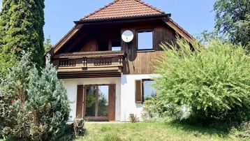 Traditionelles Einfamilienhaus mit Holzfassade und Balkon, umgeben von viel Grün.