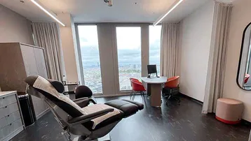 Modernes Behandlungszimmer mit bequemer Liege, Schreibtisch und weitem Blick über die Stadt.