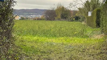 Blick auf ein grünes Feld oder Baugrundstück mit Hügeln im Hintergrund unter bewölktem Himmel.