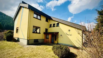 Gelbes Einfamilienhaus mit schrägem Dach und dekorativen Elementen an der Fassade.