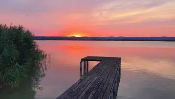 Malerischer Sonnenuntergang über dem See mit einem Holzsteg und Schilf im Vordergrund.