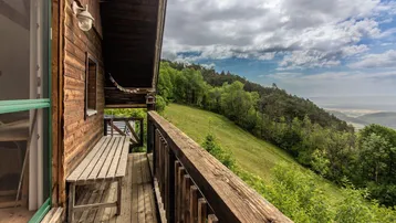 Rustikaler Holzbalkon mit Sitzbank und weitem Blick über die bewaldete Landschaft und das Tal.