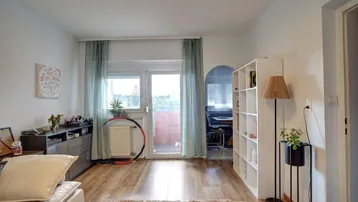 Helles Wohnzimmer mit Laminatboden, Balkonzugang und einem Durchgang zu einem weiteren Raum.