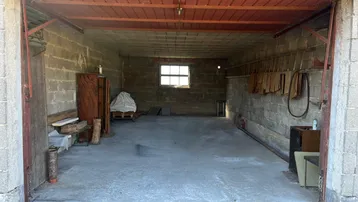 Geräumige Garage mit Betonwänden und -boden, offenem Tor und einem kleinen Fenster im hinteren Bereich.