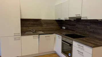Moderne Einbauküche mit weißen Schränken, dunkler Arbeitsplatte und integrierten Geräten in hellem Raum.
