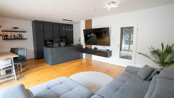 Geräumiger Wohnbereich mit bequemer Couch, moderner Küche und Zugang zum Außenbereich.