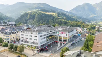 Luftaufnahme eines Geschäftskomplexes in einer Stadt, umgeben von grünen Hügeln und Bergen.