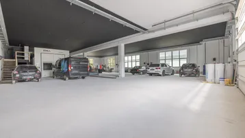 Große, helle Werkstatt mit hohen Decken, Betonboden und mehreren Fahrzeugen sowie Arbeitsgeräten.