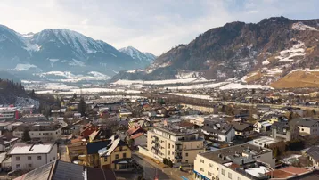 Luftaufnahme einer Stadt mit schneebedeckten Bergen im Hintergrund und vielen Wohnhäusern.