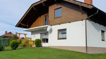 Traditionelles Haus mit Holzelementen, weißer Fassade und gepflegtem Rasen.