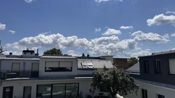 Blick auf den gepflegten Gartenbereich mit Rasenfläche und angrenzenden modernen Gebäuden unter blauem Himmel.