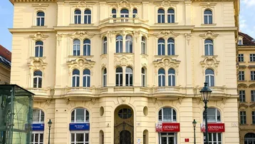 Prächtiges historisches Gebäude mit klassischer Architektur und moderner Dachaufstockung in einer Stadtansicht.