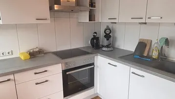 Moderne Küche mit weißen Schränken, dunkler Arbeitsplatte und Parkettboden unter Holzbalken.