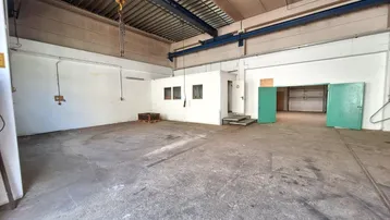 Geräumige Lagerhalle mit Betonboden, hohen Decken und einem blauen Laufkran für schwere Lasten.