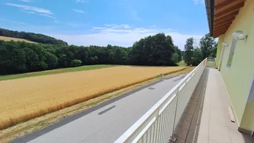 Langer Balkon mit Fliesenboden und weitem Blick über goldene Felder und grüne Wälder.