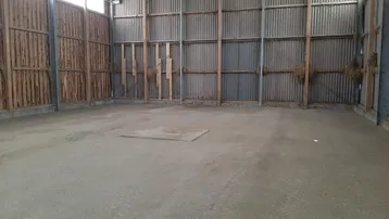 Großer leerer Innenraum mit Betonboden, Wellblechwänden und Holzverkleidung, ideal als Lagerfläche.