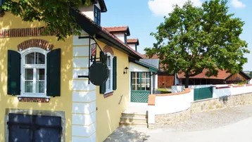 Traditionelles Gebäude mit gelber Fassade, grünen Fensterläden und einem Eingangsbereich unter Bäumen.