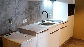 Kleine, moderne Küche mit weißen Schränken, Induktionskochfeld, Mikrowelle und integrierter Waschmaschine.
