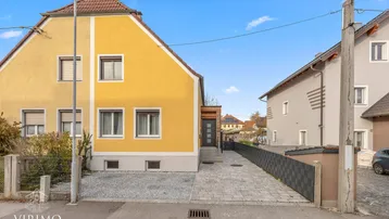 Gelbes Einfamilienhaus mit gepflasterter Einfahrt, Vorgarten und Satteldach.