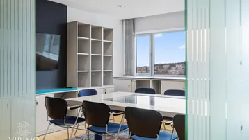 Moderner Konferenzraum mit großem Tisch, blauen Stühlen und Blick auf die Stadt.