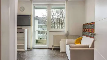 Helles Wohnzimmer mit Sofa, Fernseher und Zugang zu einem kleinen Balkon.