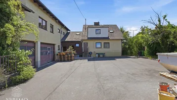 Gebäudeansicht mit großem gepflasterten Vorplatz und angrenzenden Garagen unter blauem Himmel.