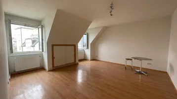 Helles Dachgeschosszimmer mit Holzboden, schrägen Wänden und zwei Fenstern, ideal als Wohn- oder Schlafzimmer.