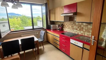 Küche mit roten und holzfarbenen Schränken, Esstisch und schöner Aussicht.