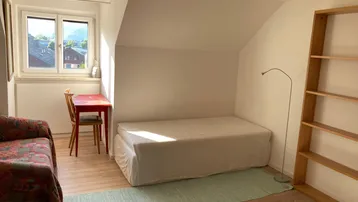 Helles Schlafzimmer mit Dachschräge, Holzboden und Blick auf die umliegende Landschaft.