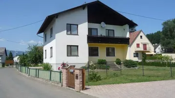 Einfamilienhaus mit weißer Fassade, Balkon und gepflegtem Vorgarten in ländlicher Umgebung.