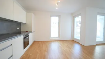 Helle Wohnküche mit modernen weißen Schränken, integriertem Backofen und Parkettboden.