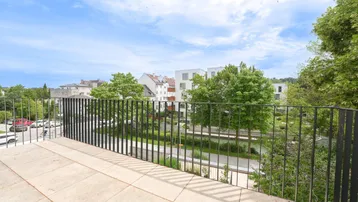 Geräumiger Balkon mit Fliesenboden und Blick auf die grüne Umgebung und moderne Gebäude.