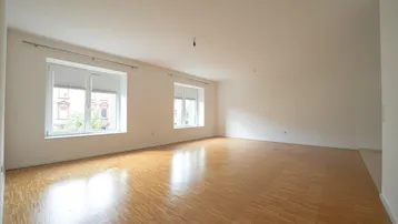 Helles, leeres Zimmer mit Parkettboden und zwei Fenstern, bereit zur individuellen Gestaltung.